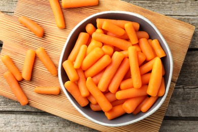 Baby carrots in bowl on wooden table, top view