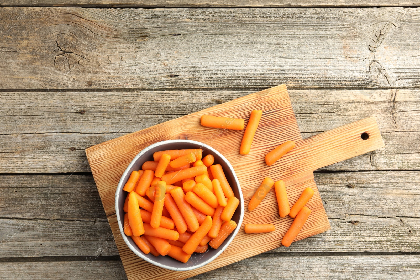 Photo of Baby carrots in bowl on wooden table, top view