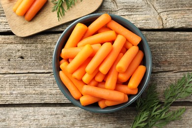 Photo of Baby carrots in bowl and green leaves on wooden table, top view