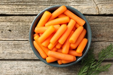 Baby carrots in bowl and green leaf on wooden table, top view