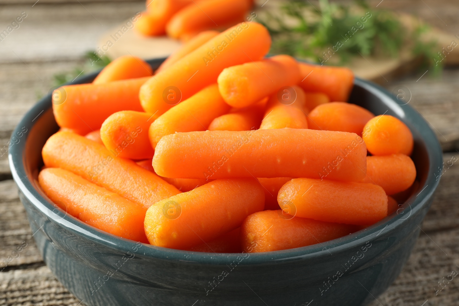 Photo of Baby carrots in bowl on wooden table, closeup