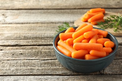 Baby carrots in bowl and green leaves on wooden table, space for text