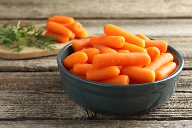 Baby carrots in bowl and green leaves on wooden table