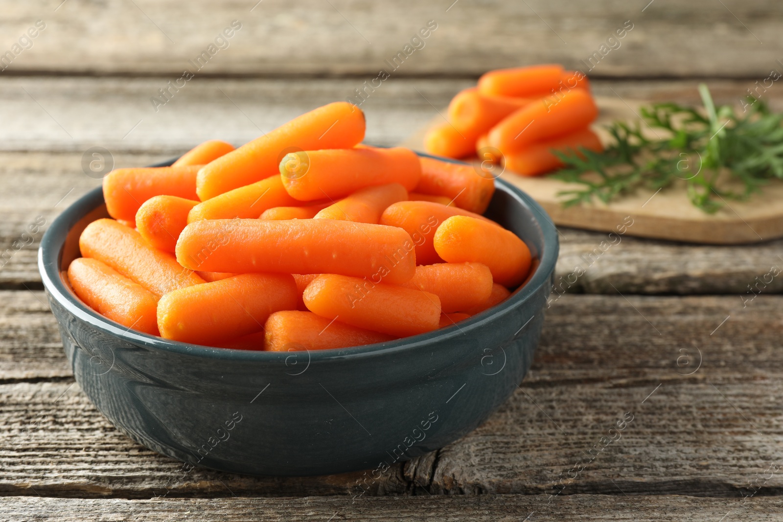 Photo of Baby carrots in bowl and green leaves on wooden table