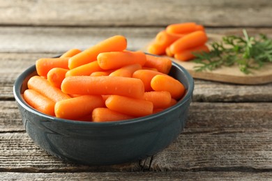 Photo of Baby carrots in bowl and green leaves on wooden table