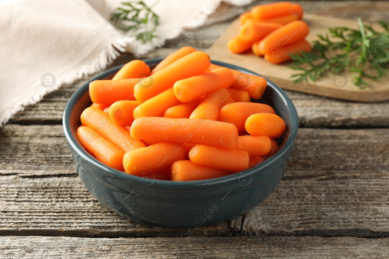 Photo of Baby carrots in bowl and green leaves on wooden table