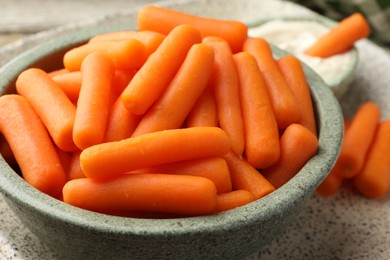 Photo of Baby carrots in bowl and sauce on table, closeup