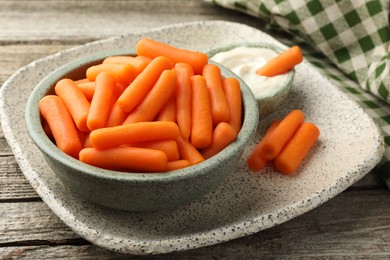 Baby carrots in bowl and sauce on wooden table