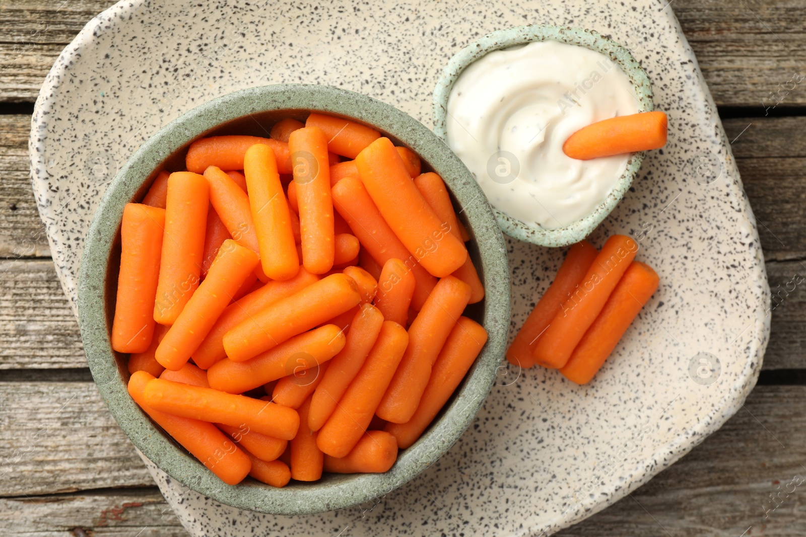 Photo of Baby carrots in bowl and sauce on wooden table, top view