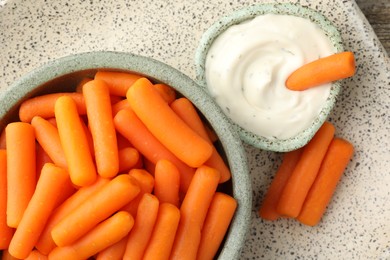 Photo of Baby carrots in bowl and sauce on table, top view