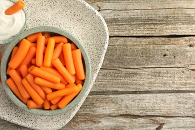 Photo of Baby carrots in bowl and sauce on wooden table, top view. Space for text