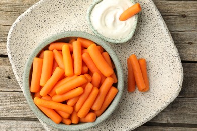 Photo of Baby carrots in bowl and sauce on wooden table, top view