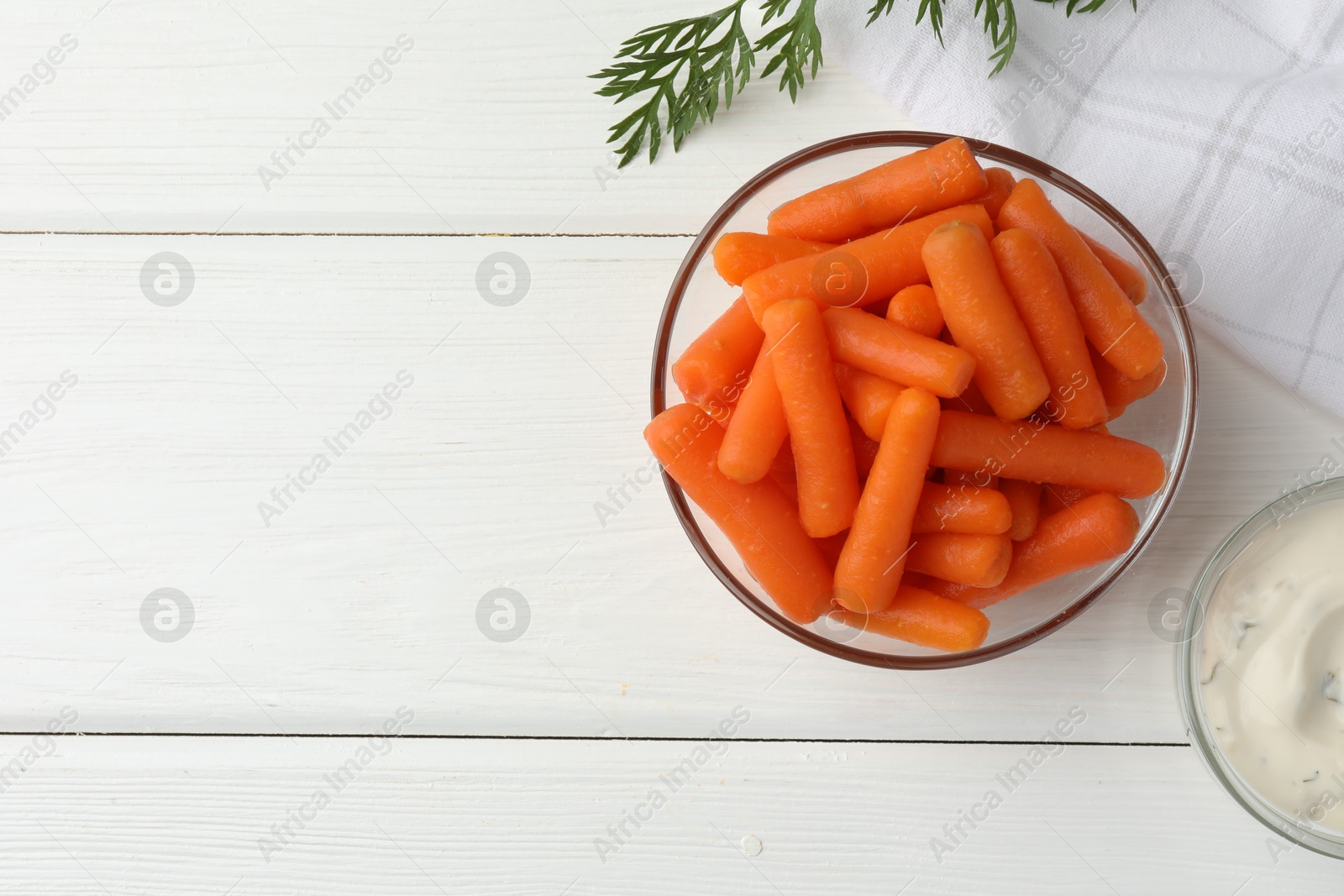 Photo of Baby carrots in bowl, sauce and green leaf on white wooden table, top view. Space for text