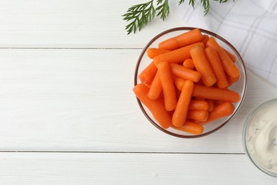 Baby carrots in bowl, sauce and green leaf on white wooden table, top view. Space for text