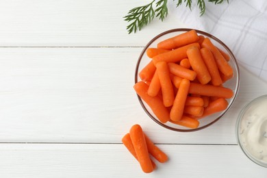 Photo of Baby carrots in bowl, sauce and green leaf on white wooden table, top view. Space for text