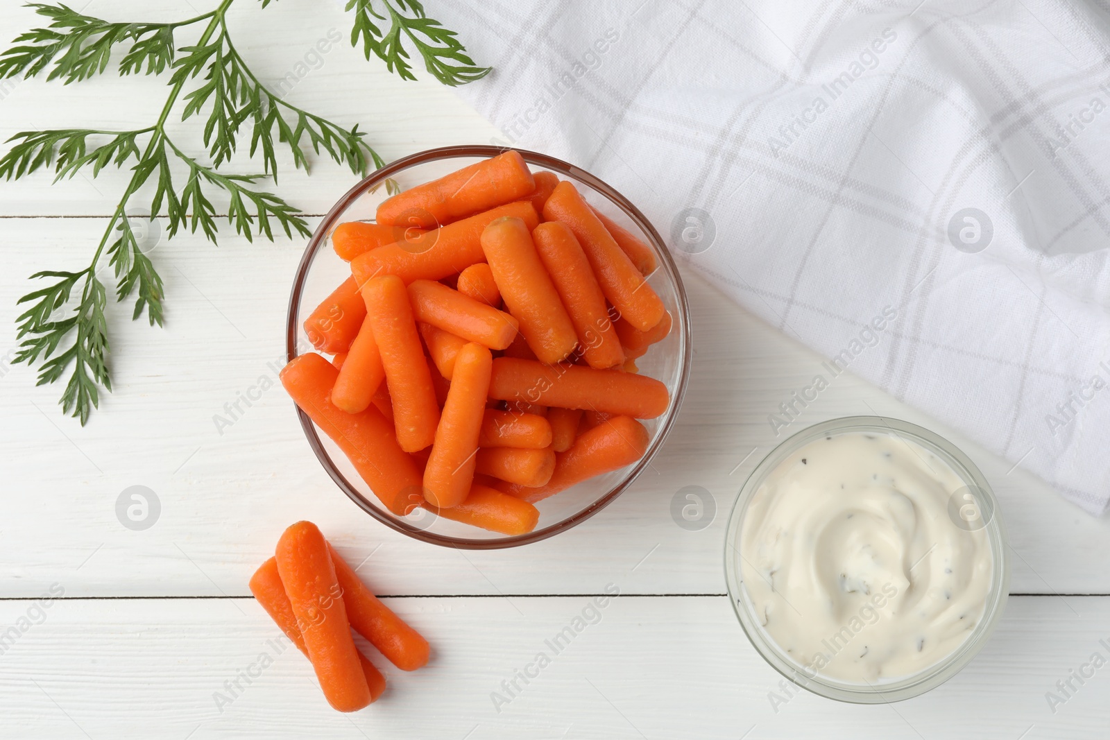 Photo of Baby carrots in bowl, sauce and green leaf on white wooden table, top view