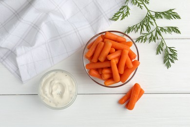 Photo of Baby carrots in bowl, sauce and green leaf on white wooden table, top view