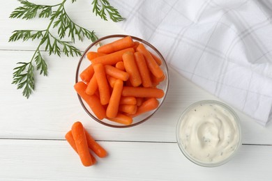 Photo of Baby carrots in bowl, sauce and green leaf on white wooden table, top view