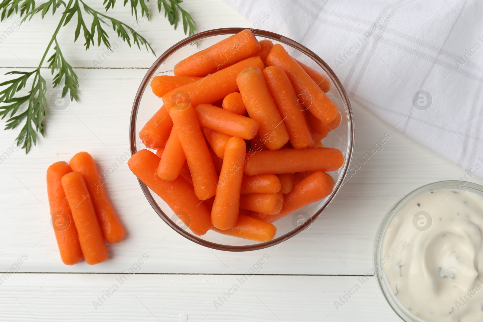 Photo of Baby carrots in bowl, sauce and green leaf on white wooden table, top view