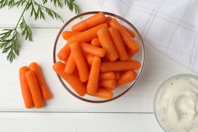 Photo of Baby carrots in bowl, sauce and green leaf on white wooden table, top view