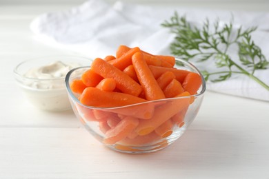 Baby carrots in glass bowl, sauce and green leaf on white wooden table