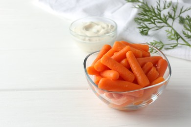 Baby carrots in glass bowl, sauce and green leaf on white wooden table, space for text