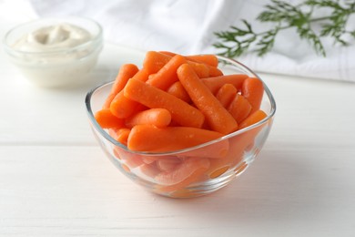 Photo of Baby carrots in glass bowl, sauce and green leaf on white wooden table