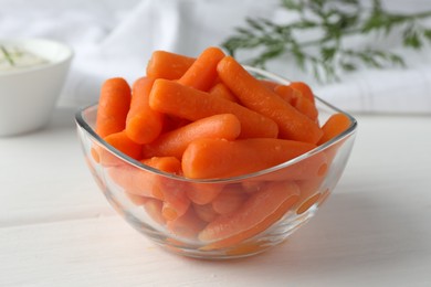 Baby carrots in glass bowl on white wooden table