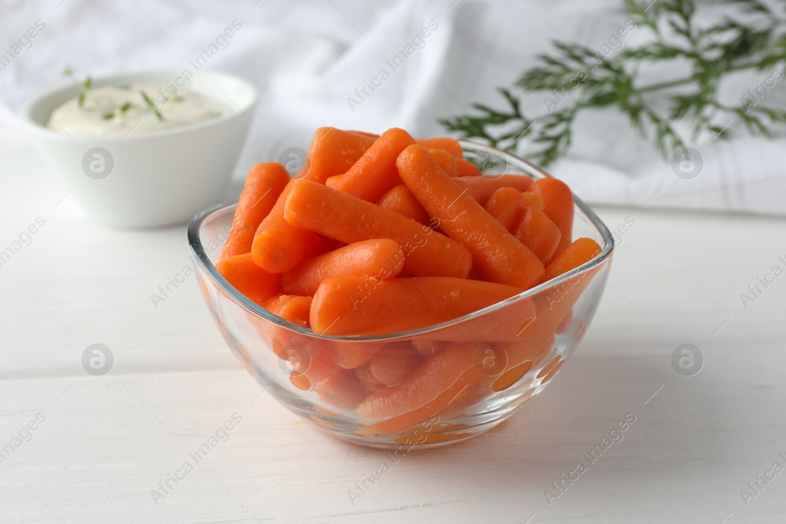 Photo of Baby carrots in glass bowl, sauce and green leaf on white wooden table