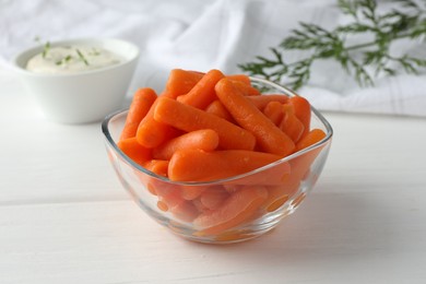 Photo of Baby carrots in glass bowl, sauce and green leaf on white wooden table