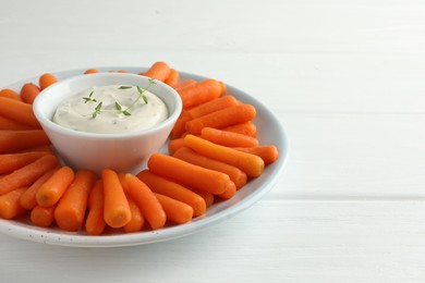 Photo of Baby carrots and sauce on white wooden table, space for text