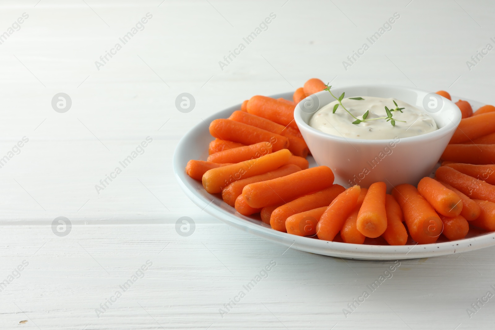 Photo of Baby carrots and sauce on white wooden table, space for text