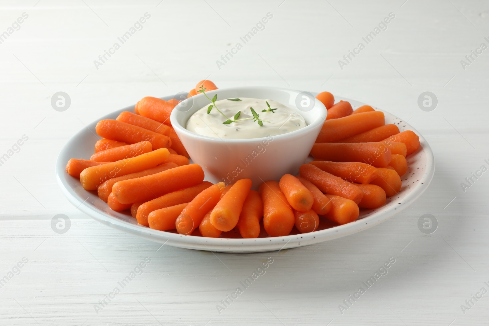 Photo of Baby carrots and sauce on white wooden table