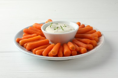 Photo of Baby carrots and sauce on white wooden table