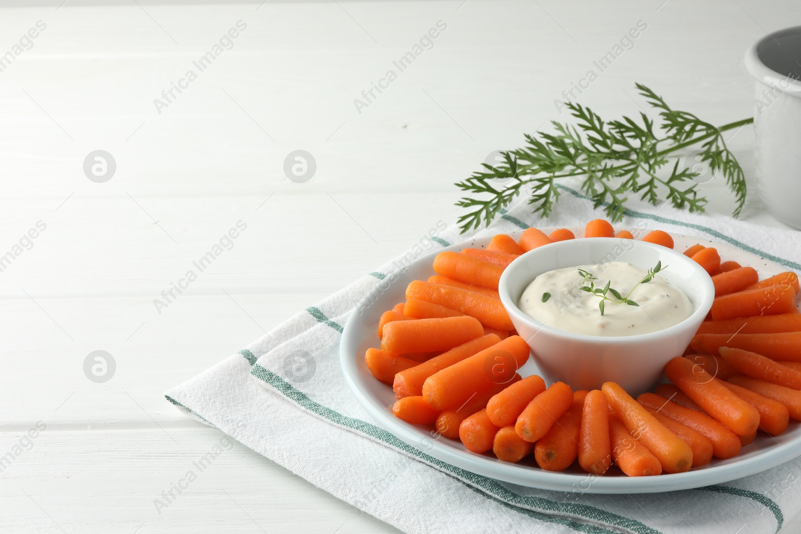 Photo of Baby carrots, sauce and green leaf on white wooden table. Space for text