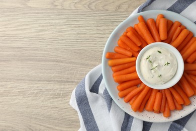 Photo of Baby carrots and sauce on wooden table, top view. Space for text