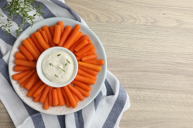 Baby carrots and sauce on wooden table, top view. Space for text