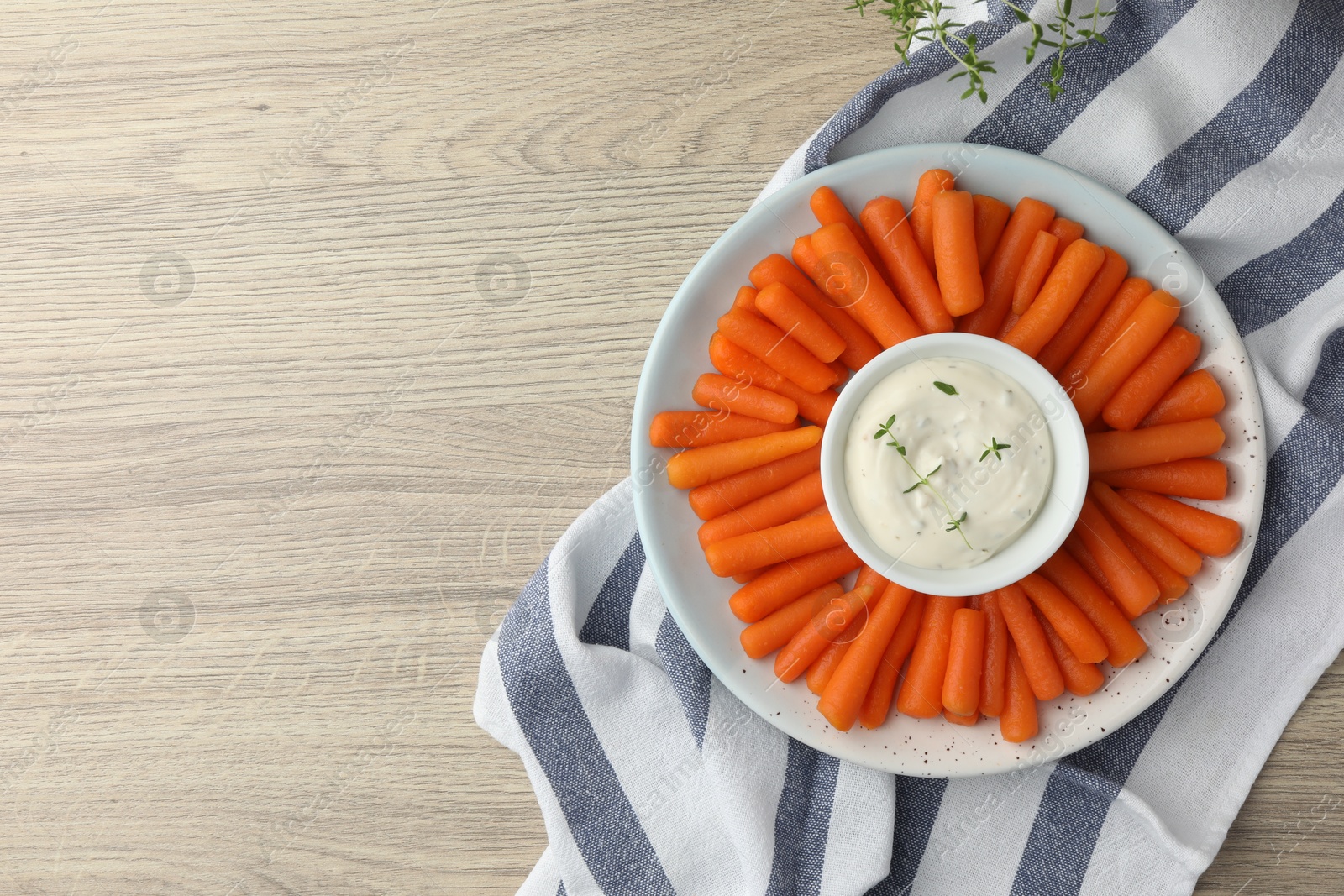 Photo of Baby carrots and sauce on wooden table, top view. Space for text