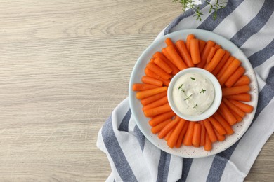 Baby carrots and sauce on wooden table, top view. Space for text