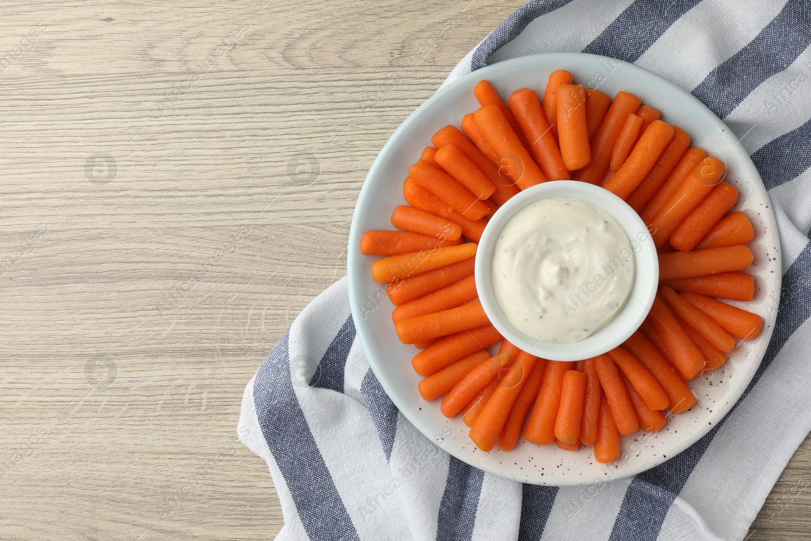 Photo of Baby carrots and sauce on wooden table, top view. Space for text