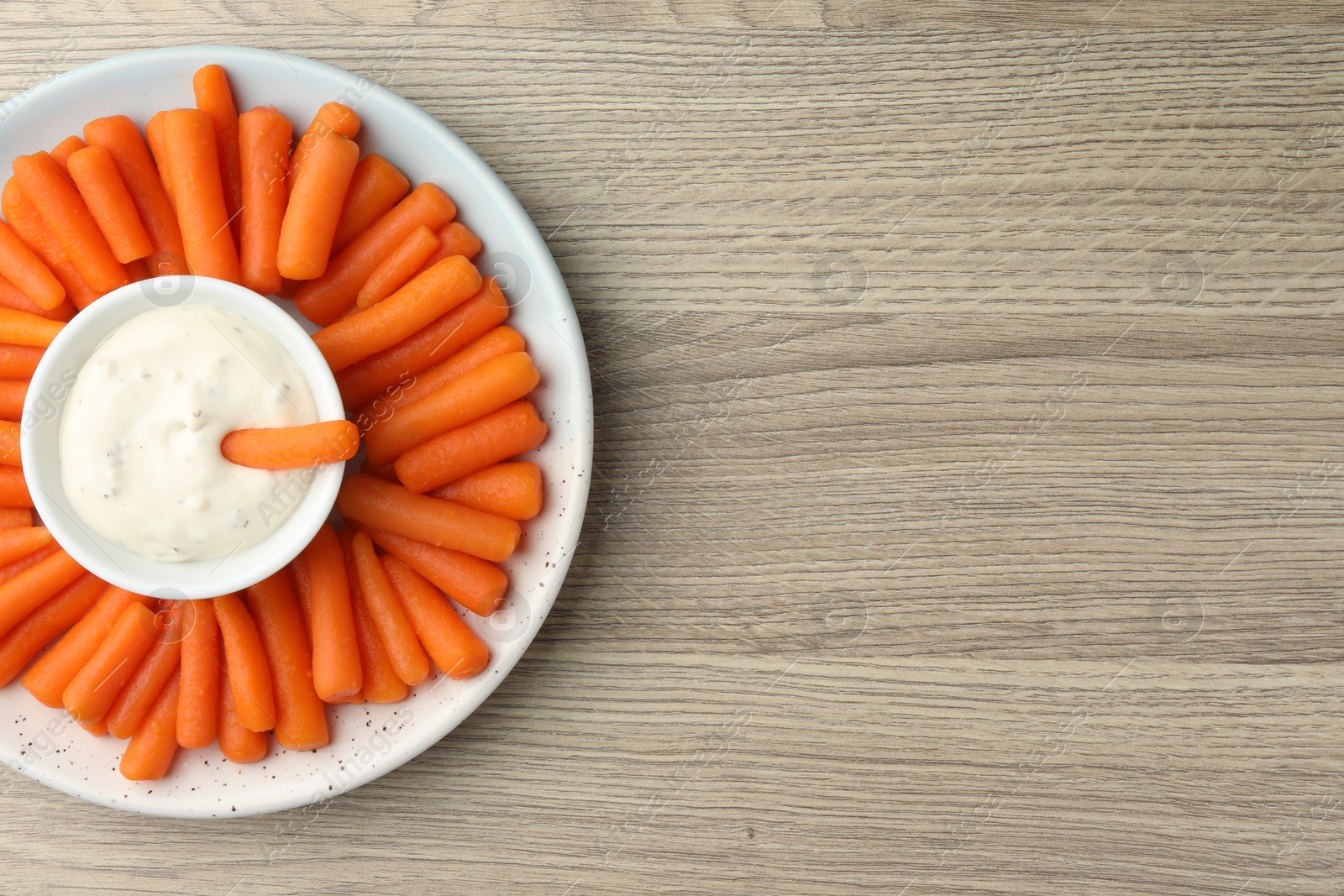 Photo of Baby carrots and sauce on wooden table, top view. Space for text