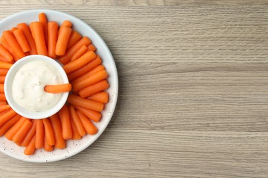 Baby carrots and sauce on wooden table, top view. Space for text