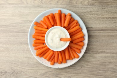 Baby carrots and sauce on wooden table, top view