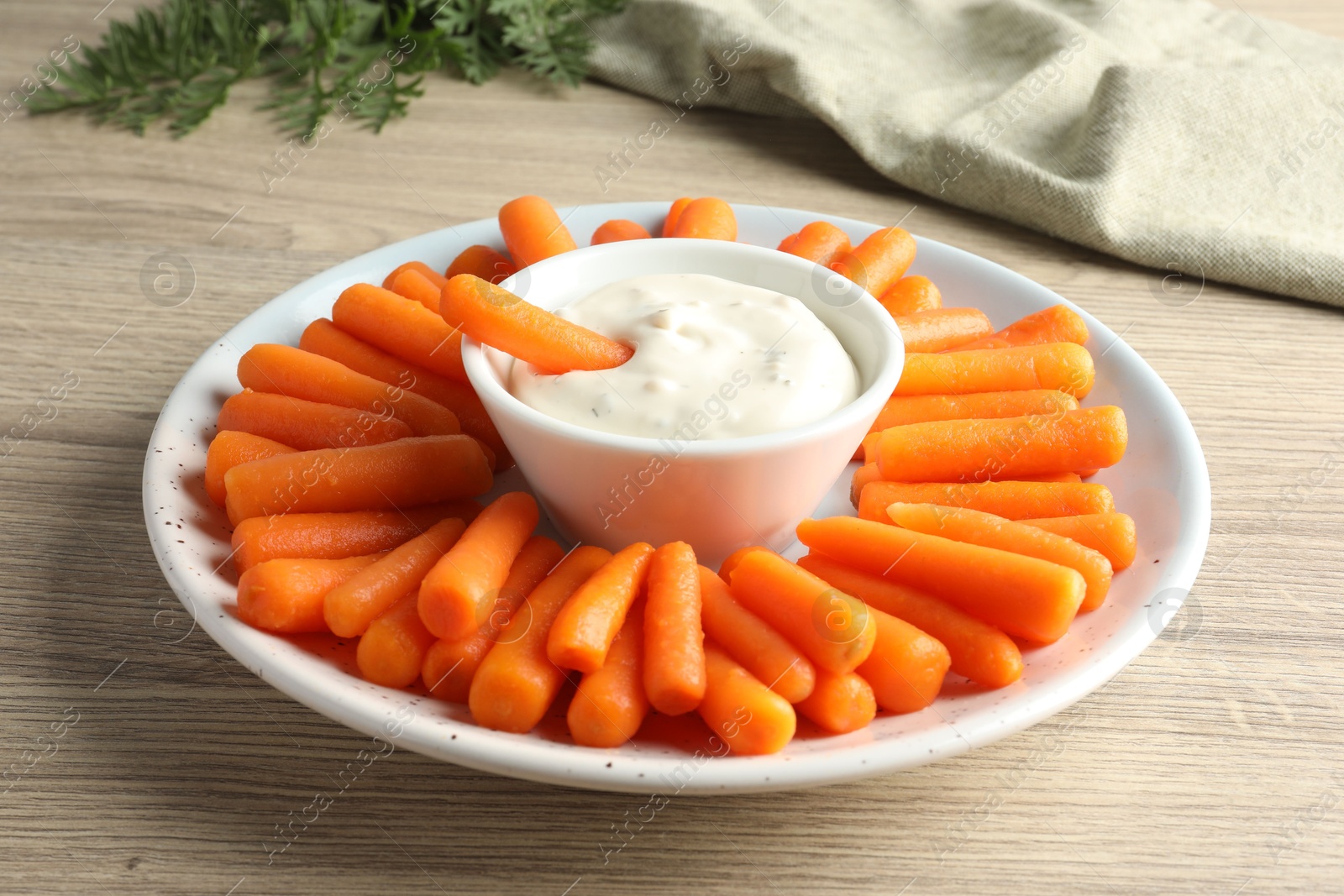 Photo of Baby carrots, sauce and green leaves on wooden table