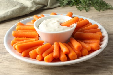 Baby carrots, sauce and green leaves on wooden table