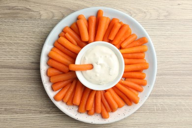 Photo of Baby carrots and sauce on wooden table, top view