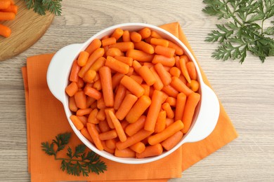 Photo of Baby carrots in pot and green leaves on wooden table, top view