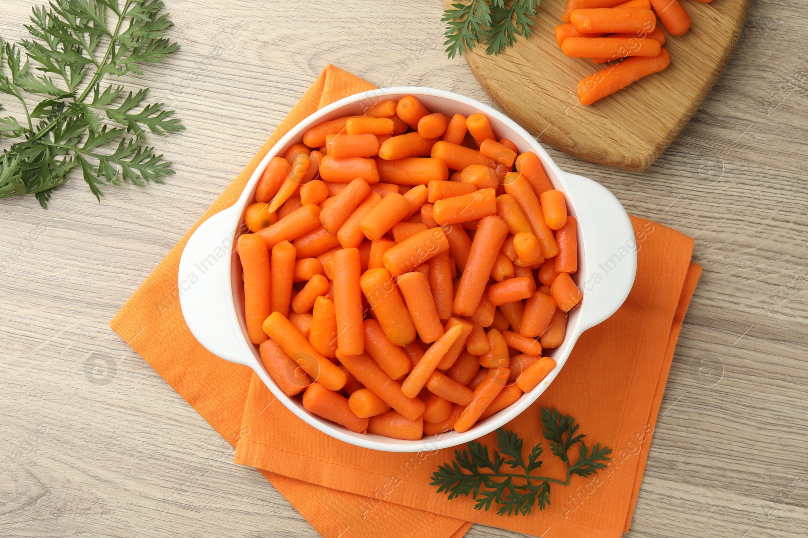 Photo of Baby carrots in pot and green leaves on wooden table, top view