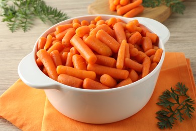 Photo of Baby carrots in pot and green leaves on wooden table