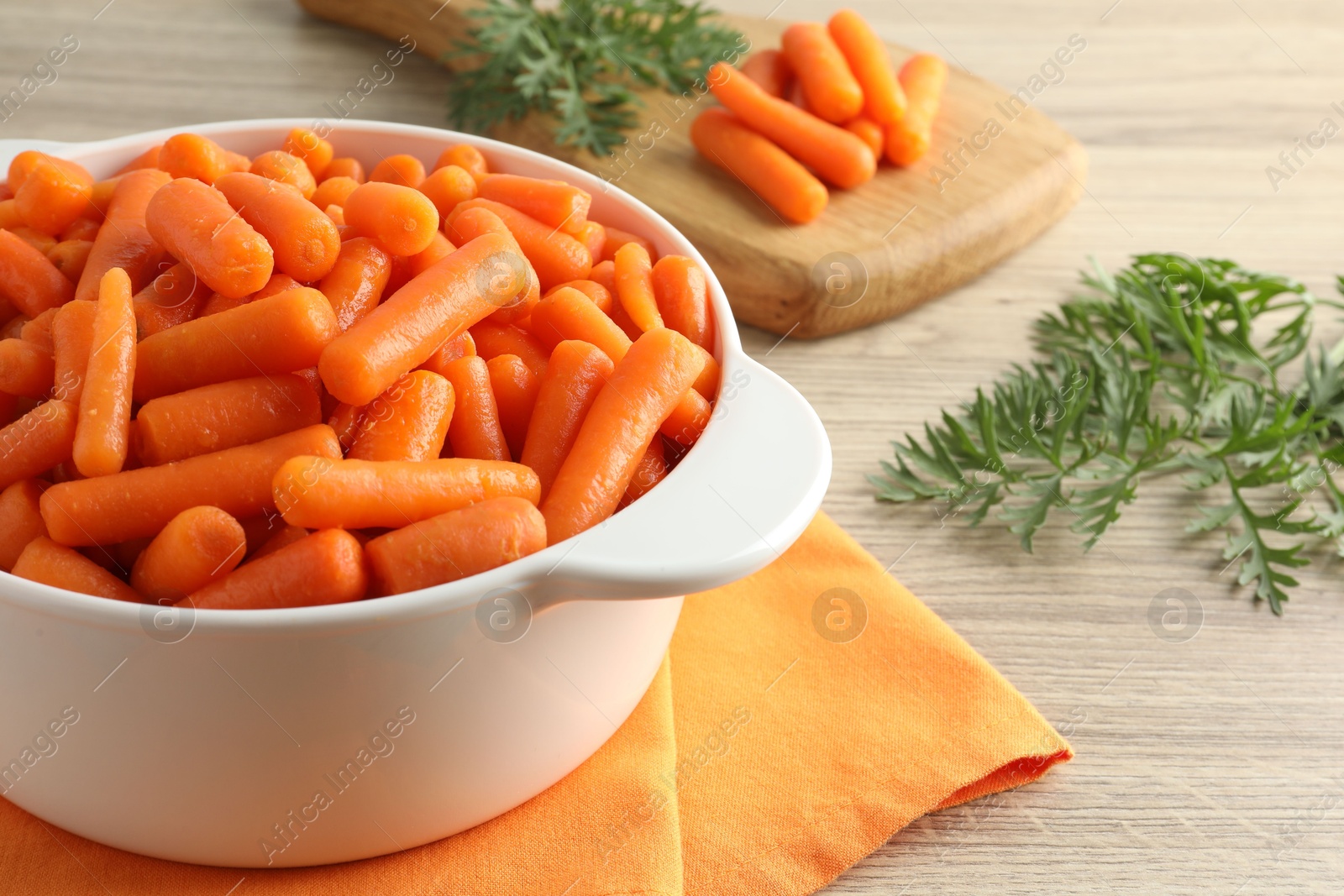 Photo of Baby carrots in pot and green leaves on wooden table